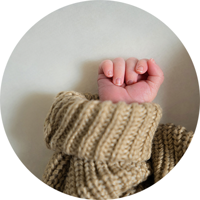 Close up of a newborn baby's clenched fist, poking out from a chunky knit jumper.