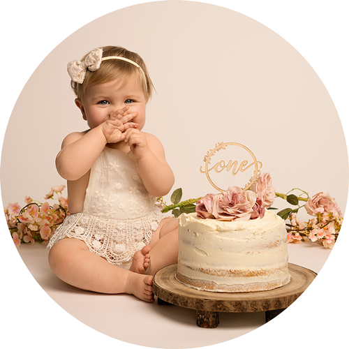 First birthday cake smash portrait of a baby girl sitting beside a floral cake, photographed in a soft, neutral style at a Hampshire cake smash photography studio.