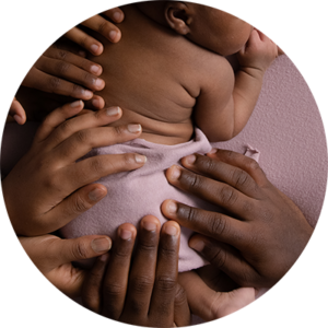 Close up of the hands of a family placed on their newborn baby's back.