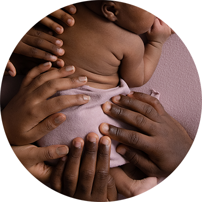 Close up of the hands of a family placed on their newborn baby's back.
