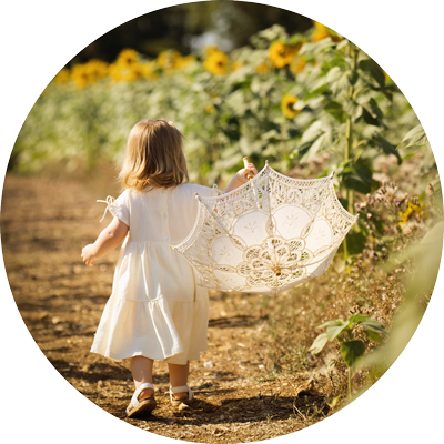 Young child walking through a sunflower field holding a lace umbrella during a golden hour photoshoot in Hampshire.