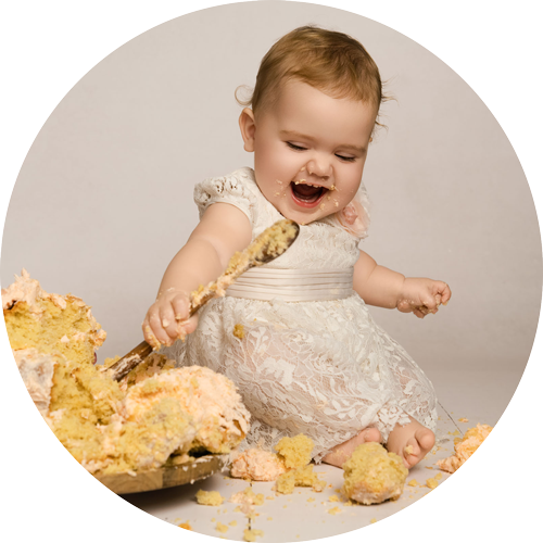 Laughing baby girl smashing her birthday cake during a first birthday cake smash photoshoot in a Hampshire studio near Andover.