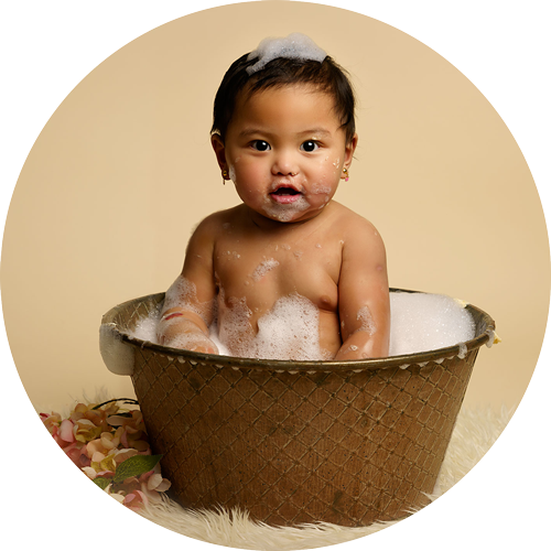 Baby girl sitting in a vintage bath surrounded by bubbles during a cake smash and splash photoshoot in Hampshire near Andover.