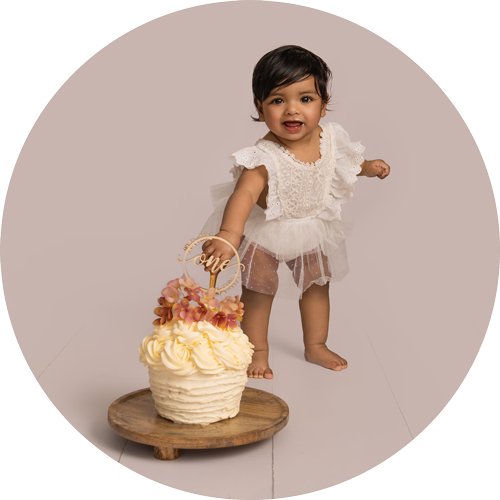 Smiling one-year-old girl standing beside her birthday cake during a cake smash photoshoot in a Hampshire photography studio near Andover.