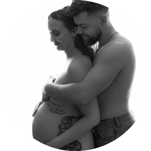 Black and white maternity portrait of an expectant couple embracing and holding their baby bump during a studio photoshoot.