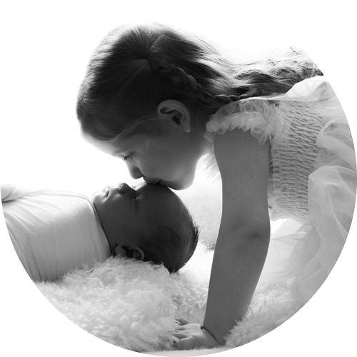 Black and white portrait of a young sister gently kissing her newborn baby sibling during a newborn photography session, captured by a Hampshire newborn photographer serving Basingstoke and surrounding areas.