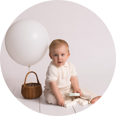 Baby sitting with a white balloon during a first birthday cake smash photoshoot near Andover, Hampshire.