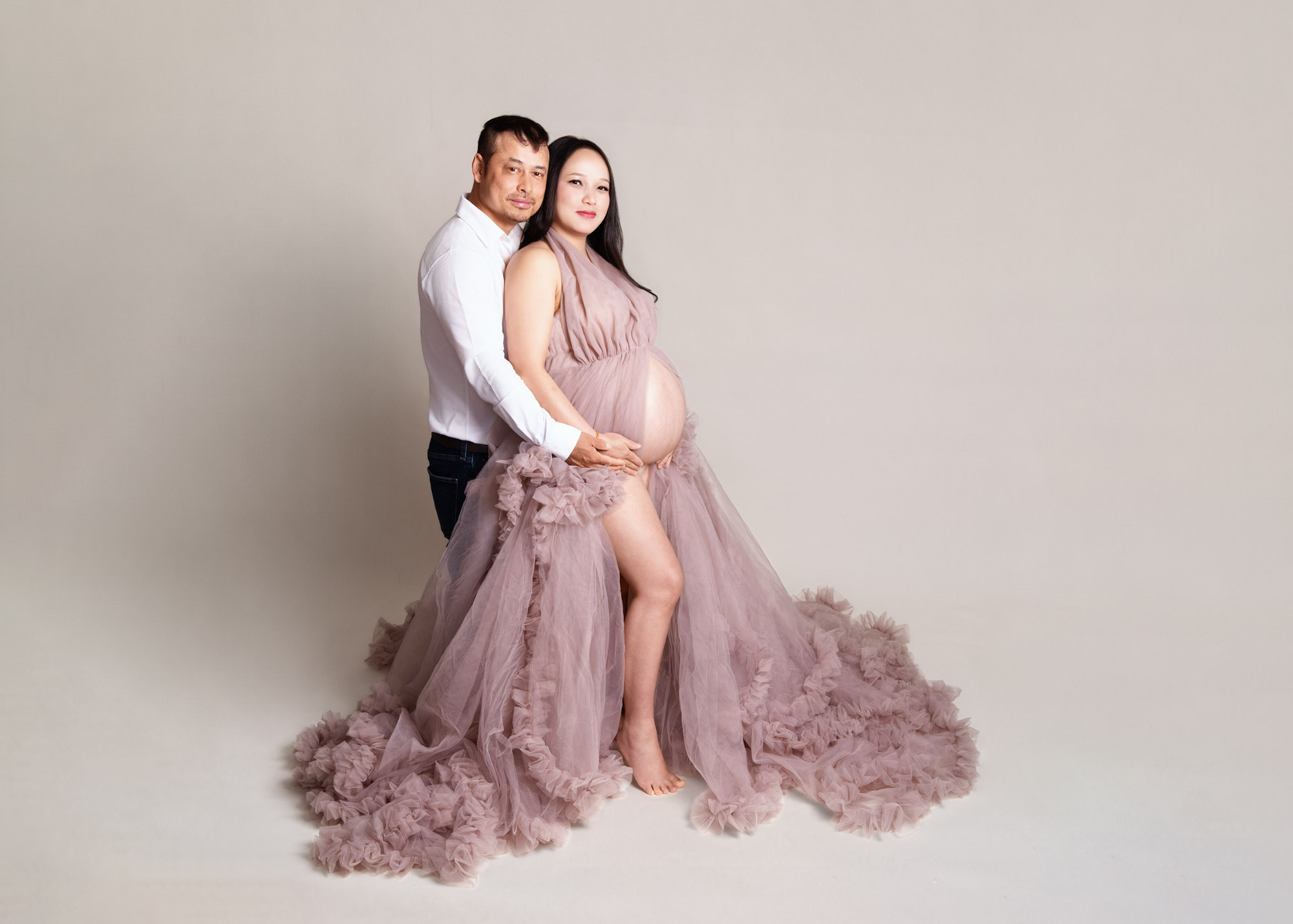 Expectant couple embracing during a maternity portrait with a pink ruffle gown