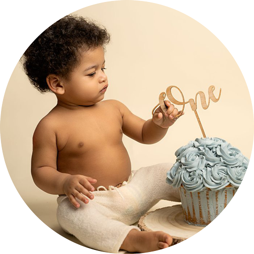Baby boy holding a ONE cake topper during his first birthday cake smash