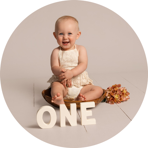 Smiling baby sitting beside ONE letters before a first birthday cake smash